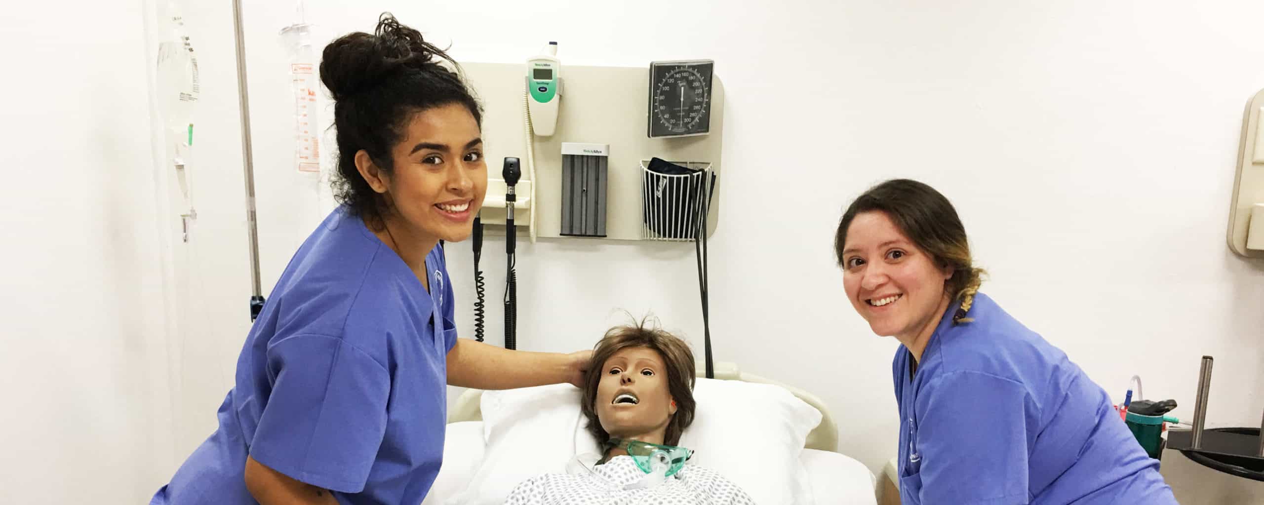 Two smiling nurses posing in lab with a patient doll